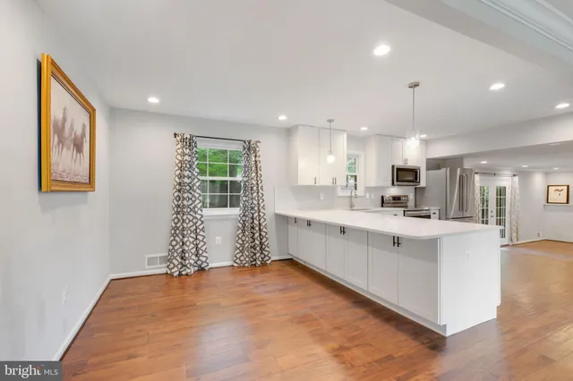a view of an empty room and kitchen with wooden floor