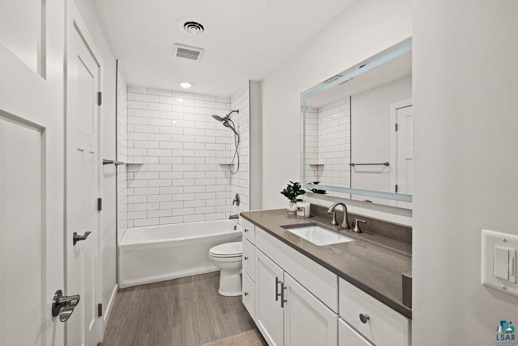 3971 Haines Road Hermantown, MN 55811 - Photo 21 of 34 Bathroom featuring a subway-tiled shower/tub combination with built-in shelving, a single vanity with a solid surface countertop, an undermount sink, and wood-finish flooring