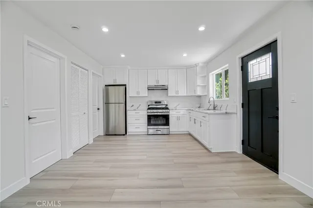 a large kitchen with a refrigerator a stove top oven a sink dishwasher and white cabinets with wooden floor