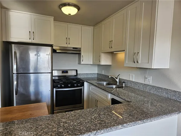 a kitchen with granite countertop a refrigerator stove and white cabinets