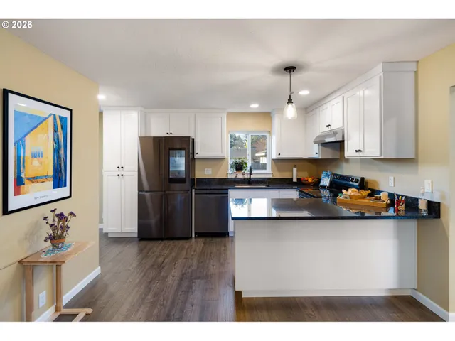 a kitchen with stainless steel appliances granite countertop a refrigerator a sink dishwasher a stove and white cabinets with wooden floor