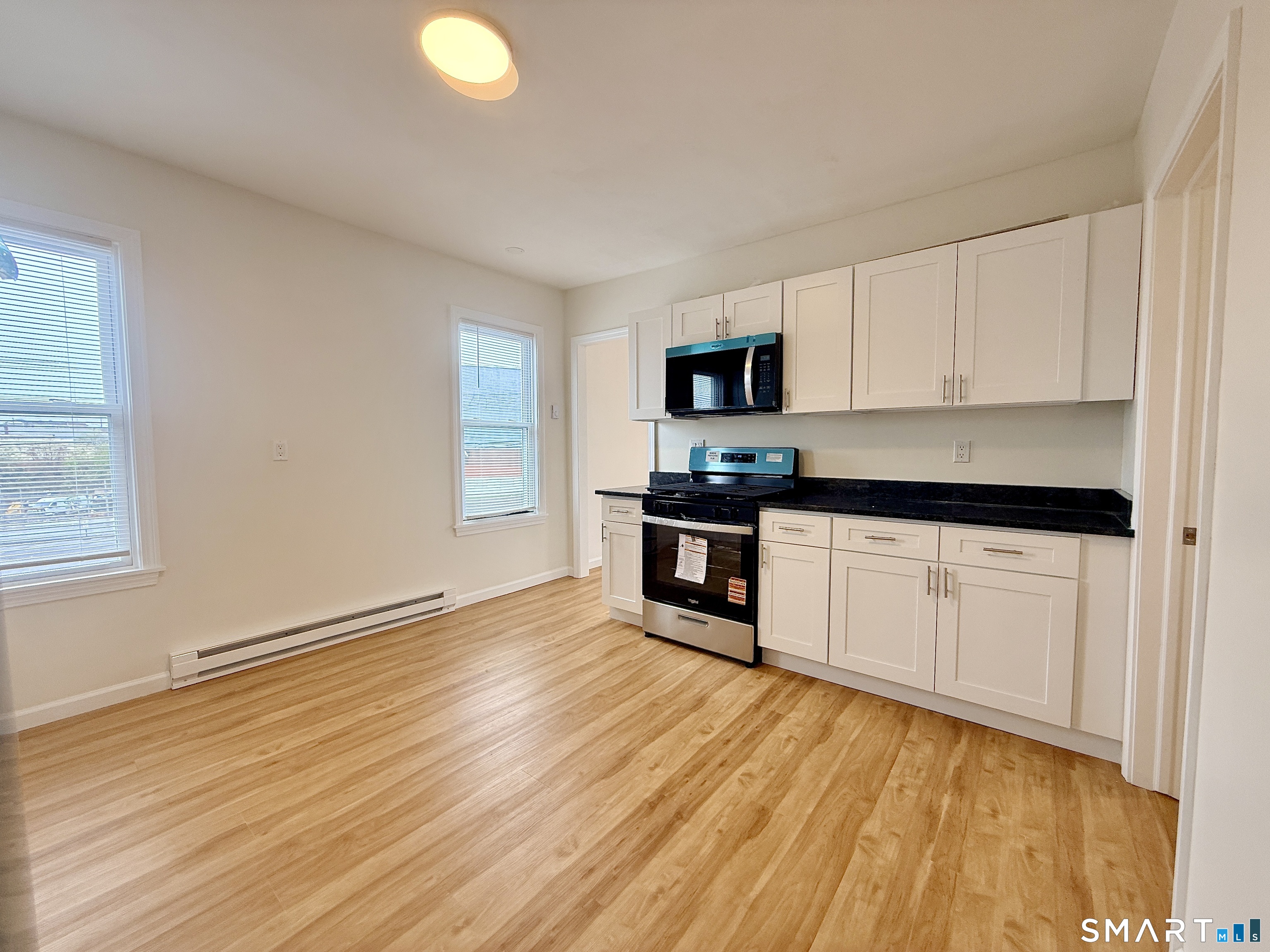 70 Lindley Street Bridgeport, CT 06604 - Photo 2 of 8 a kitchen with granite countertop a stove a sink and white cabinets with wooden floor