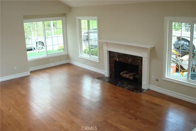 an empty room with wooden floor fireplace and windows