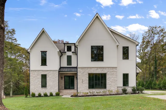 a view of a yard in front of a house with plants and large trees