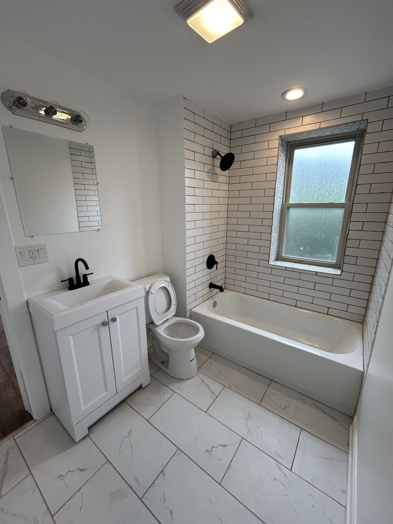 6016 South St Lawrence Avenue, Unit 1 Chicago, IL 60637 - Photo 9 of 16 a bathroom with a double vanity sink a toilet a mirror and bathtub