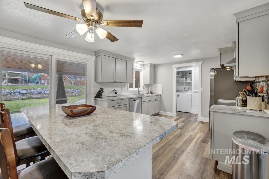 1785 River Road Buhl, ID 83316 - Photo 6 of 41 Kitchen with light countertops, gray cabinets, light wood-style flooring, backsplash, and a kitchen breakfast bar