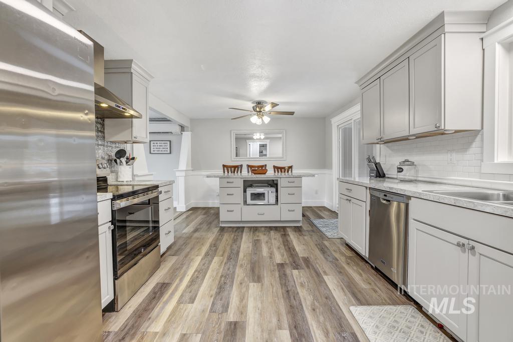 1785 River Road Buhl, ID 83316 - Photo 7 of 41 Kitchen with appliances with stainless steel finishes, tasteful backsplash, wall chimney exhaust hood, light wood-style flooring, and ceiling fan