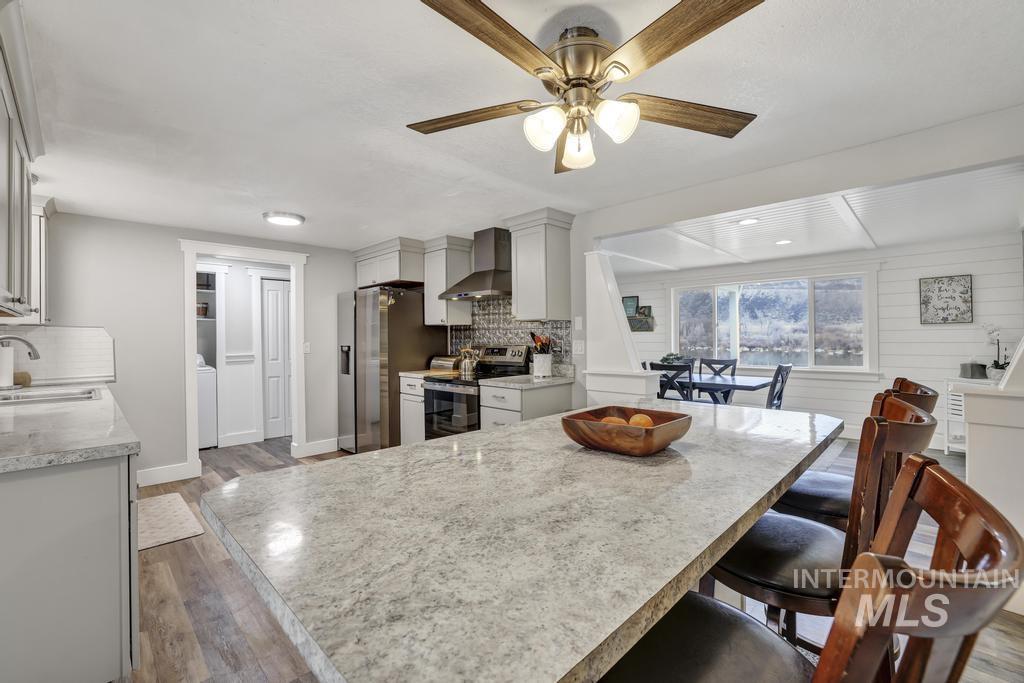 1785 River Road Buhl, ID 83316 - Photo 7 of 41 Kitchen featuring stainless steel electric stove, light wood finished floors, wall chimney exhaust hood, and a breakfast bar area
