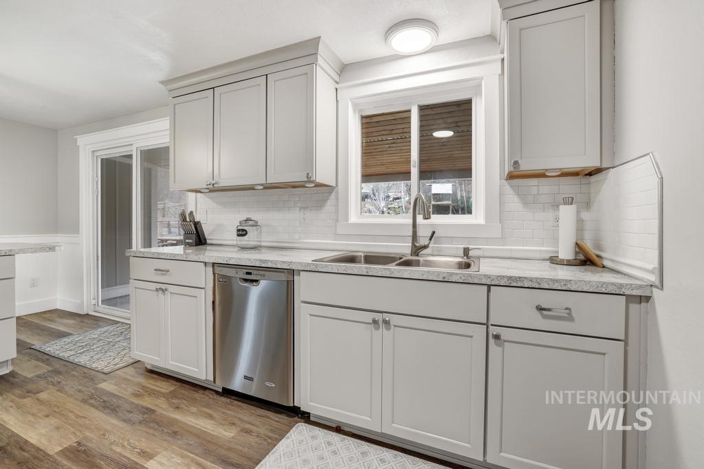 1785 River Road Buhl, ID 83316 - Photo 9 of 41 Kitchen with light countertops, stainless steel dishwasher, light wood finished floors, decorative backsplash, and a wainscoted wall