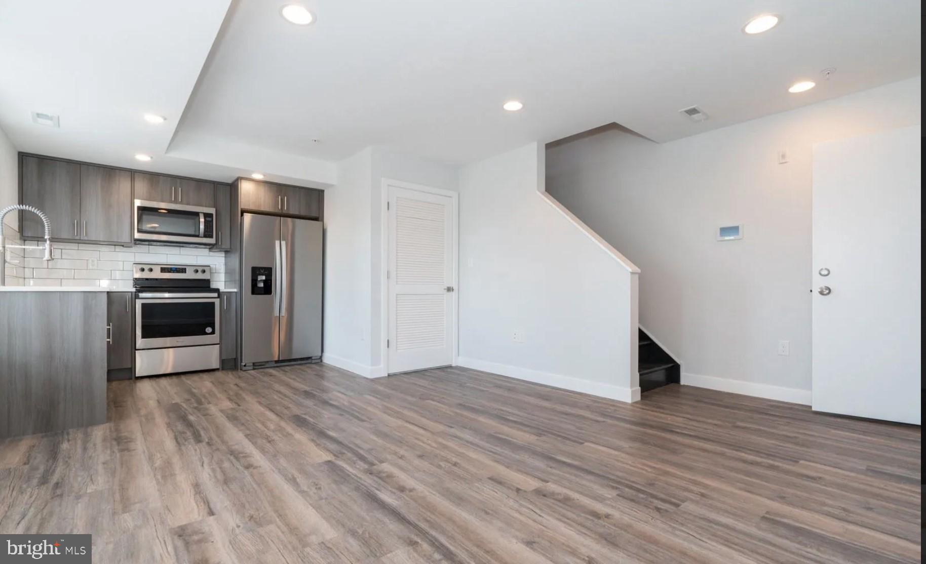 an empty room with wooden floor and stainless steel appliances