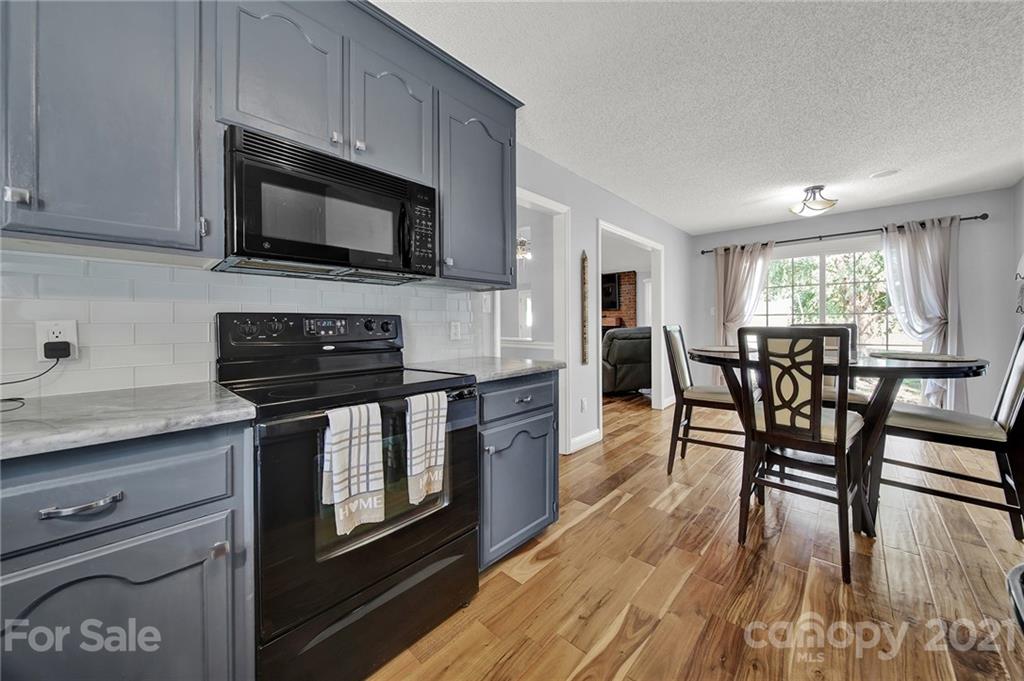 8999 West Meadow Ridge Road Indian Land, SC 29707 - Photo 20 of 28 a kitchen with stainless steel appliances granite countertop a stove top oven a sink a dining table and chairs with wooden floor