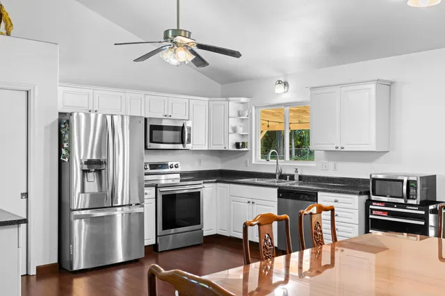 a kitchen with granite countertop a refrigerator a stove a microwave oven a sink dishwasher and a dining table with wooden floor