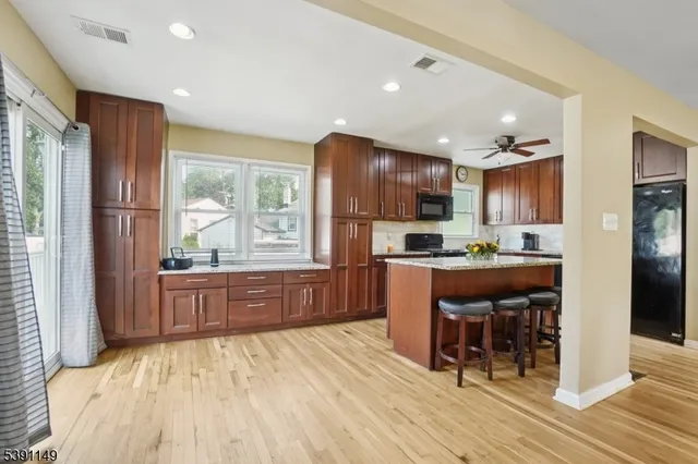 a kitchen with stainless steel appliances granite countertop a refrigerator a sink dishwasher a stove and a dining table with wooden floor