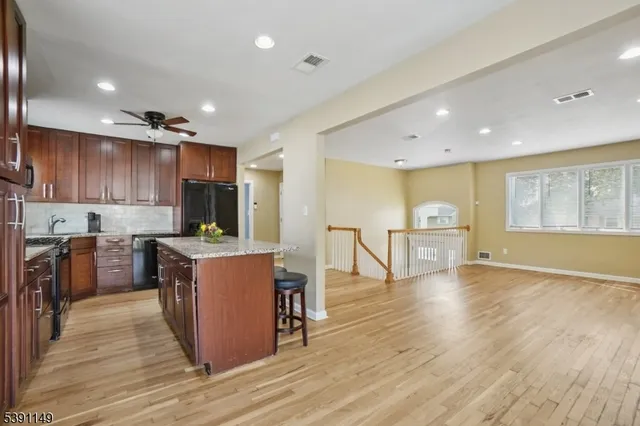 a kitchen with stainless steel appliances granite countertop a stove top oven a sink dishwasher a refrigerator and a dining table with wooden floor