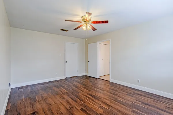 a view of an empty room with wooden floor and a ceiling fan