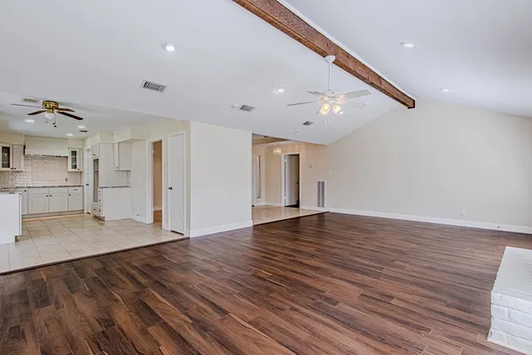 a view of an empty room with wooden floor and a kitchen