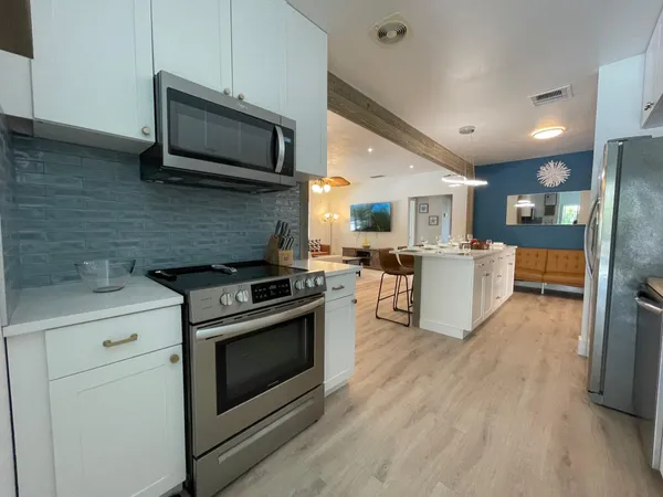 a kitchen with stainless steel appliances kitchen island granite countertop a stove top oven a sink dishwasher a refrigerator white cabinets with wooden floor