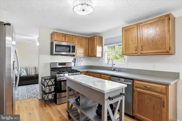 a kitchen with stainless steel appliances granite countertop a stove a refrigerator a microwave a dining table and chairs with wooden floor