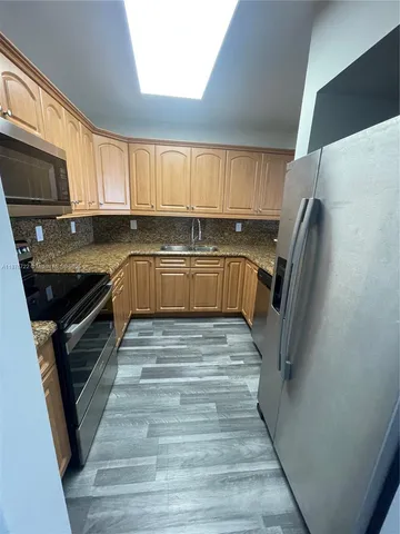 a kitchen with granite countertop a refrigerator a sink a stove and cabinets