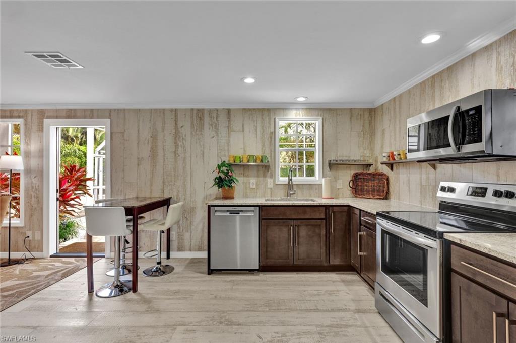 255 2nd Avenue North Naples, FL 34102 - Photo 22 of 32 a kitchen with stainless steel appliances granite countertop a stove top oven a sink dishwasher a dining table and chairs with wooden floor