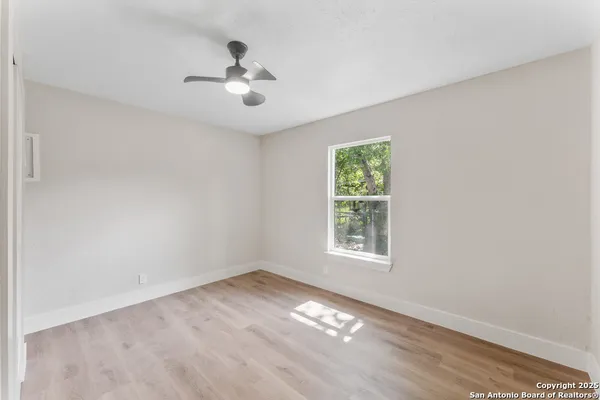 an empty room with wooden floor chandelier fan and windows