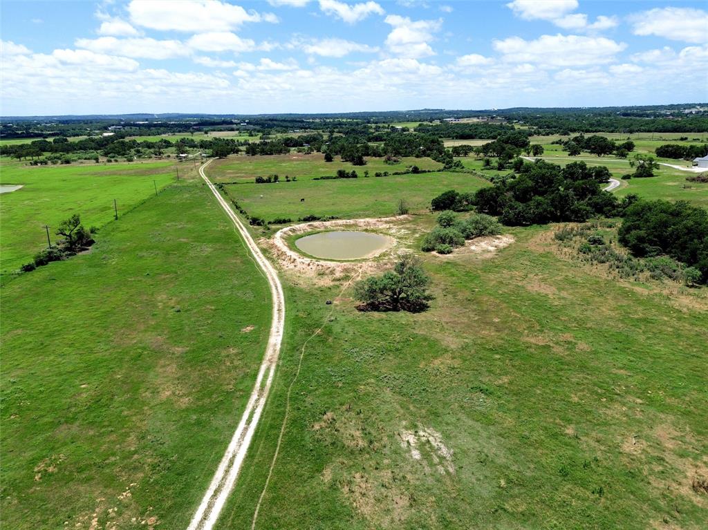 2186 Gilliland Road Springtown, TX 76082 - Photo 19 of 25 Expansive green acreage featuring a winding dirt road, scattered mature trees, and a visible pond