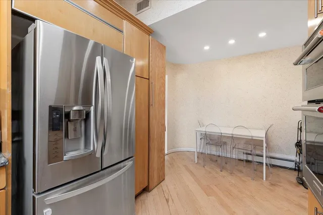 a view of a refrigerator in kitchen and an empty room with wooden floor