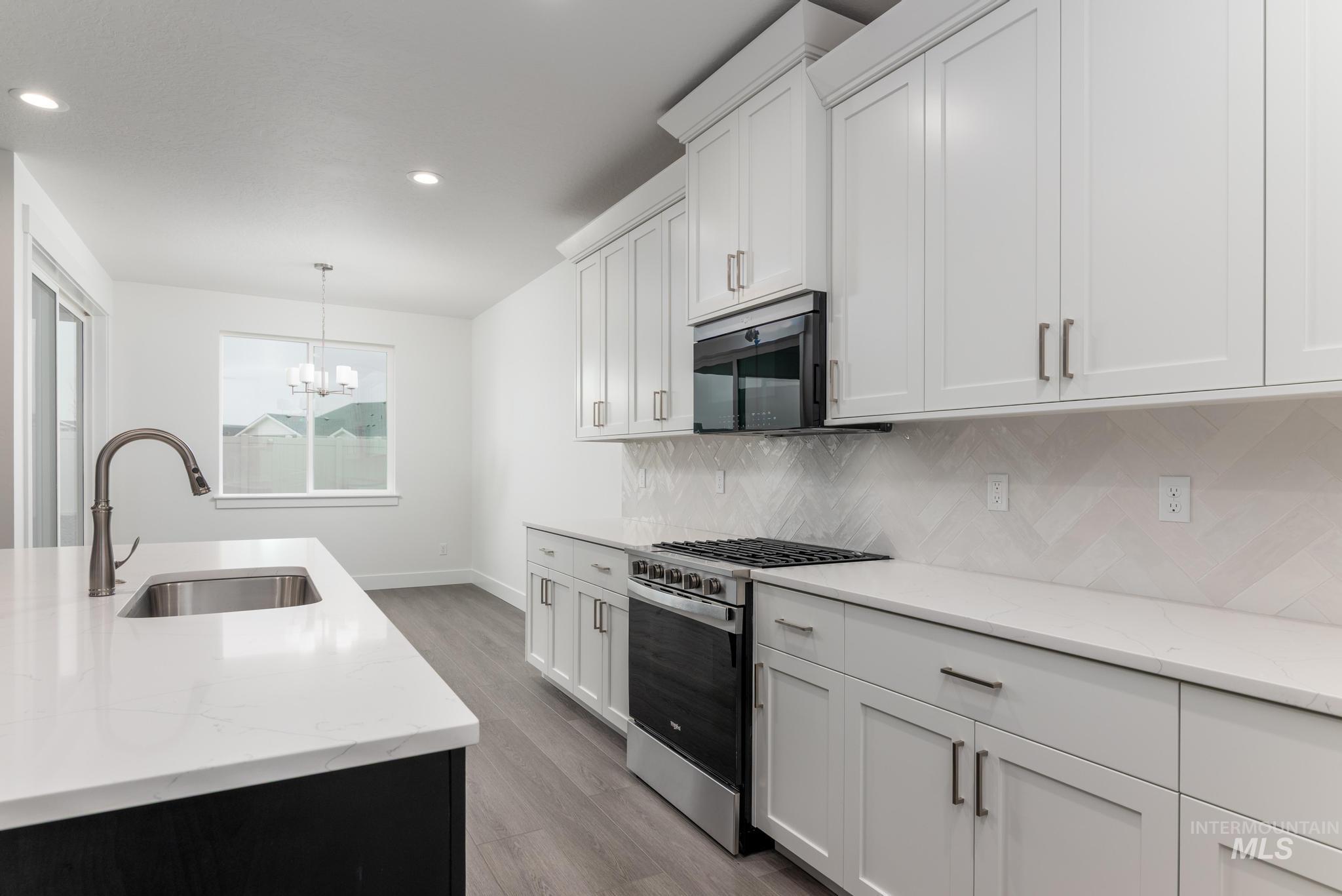 5923 West Snow Currant Street Meridian, ID 83646 - Photo 10 of 28 Kitchen with appliances with stainless steel finishes, light stone counters, light wood-style flooring, decorative light fixtures, and white cabinetry