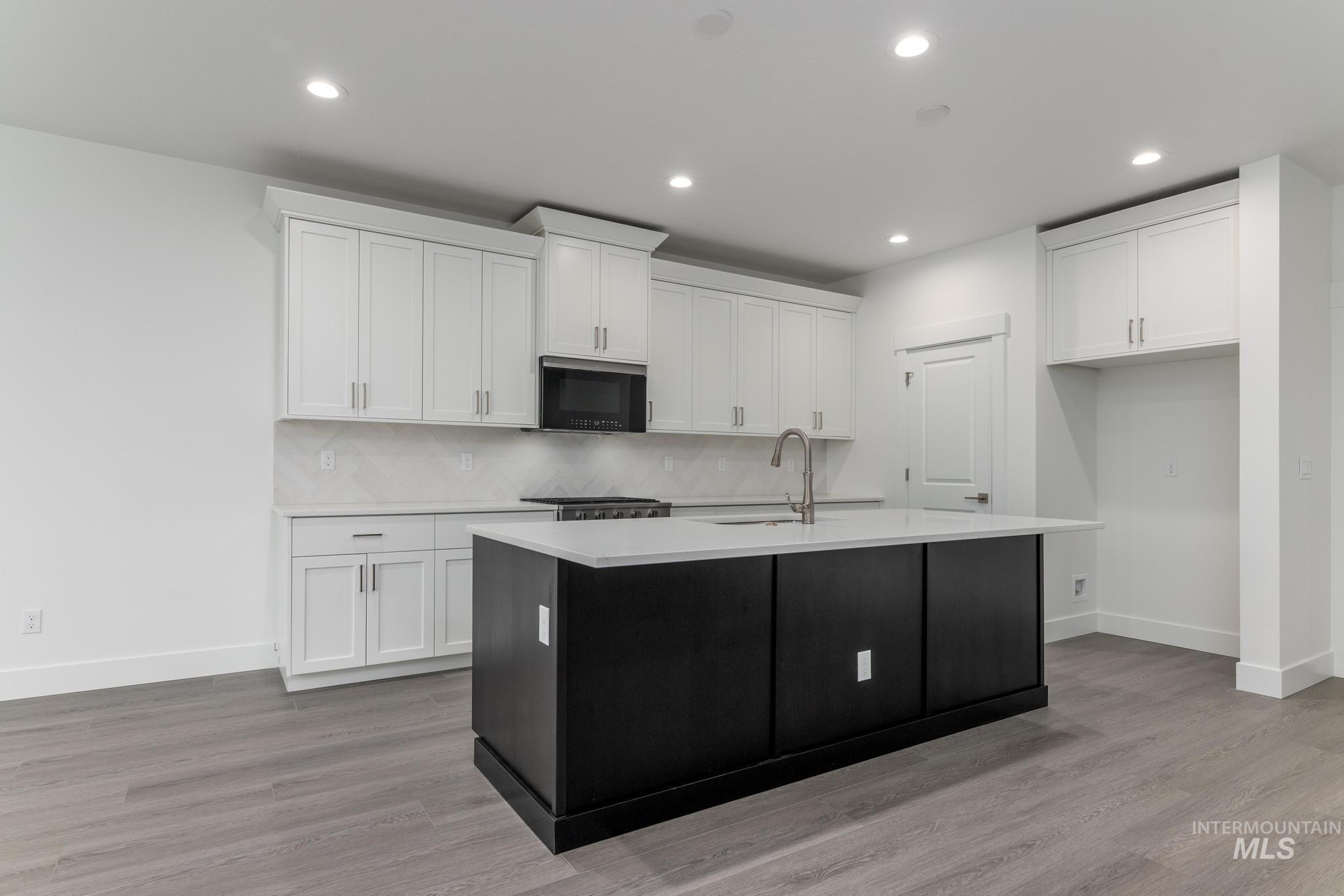 5923 West Snow Currant Street Meridian, ID 83646 - Photo 9 of 28 Kitchen with dark cabinets, a kitchen island with sink, white cabinetry, light wood-style flooring, and recessed lighting