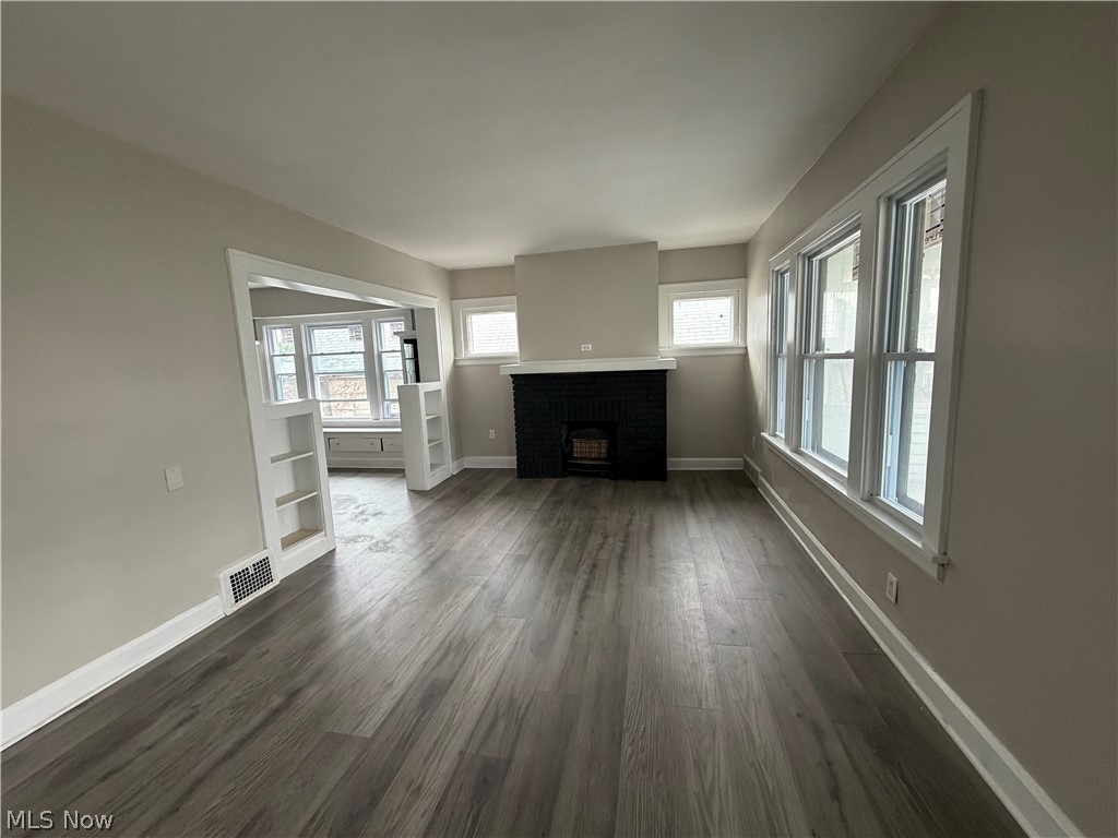 15317 Shiloh Road Cleveland, OH 44110 - Photo 19 of 29 Spacious room featuring wood-finish flooring, a decorative fireplace with a black surround, multiple windows providing natural light, and a wide entryway with built-in shelving