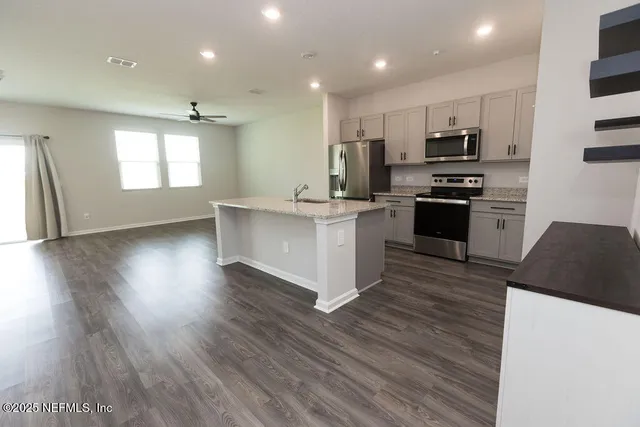 a kitchen with stainless steel appliances a stove top oven a sink a refrigerator with wooden floors and cabinets