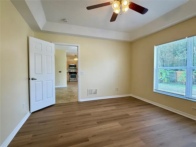 an empty room with wooden floor chandelier fan and windows