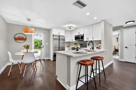 a kitchen with stainless steel appliances granite countertop a dining table chairs refrigerator and sink
