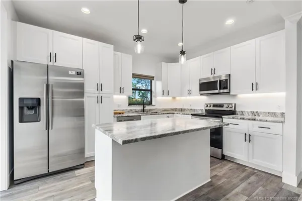 a kitchen with stainless steel appliances granite countertop a refrigerator a sink dishwasher a stove and white cabinets with wooden floor