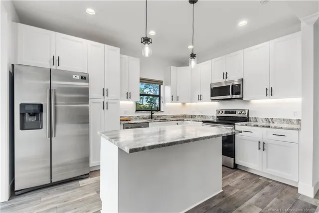 a kitchen with stainless steel appliances granite countertop a refrigerator a sink dishwasher a stove and white cabinets with wooden floor