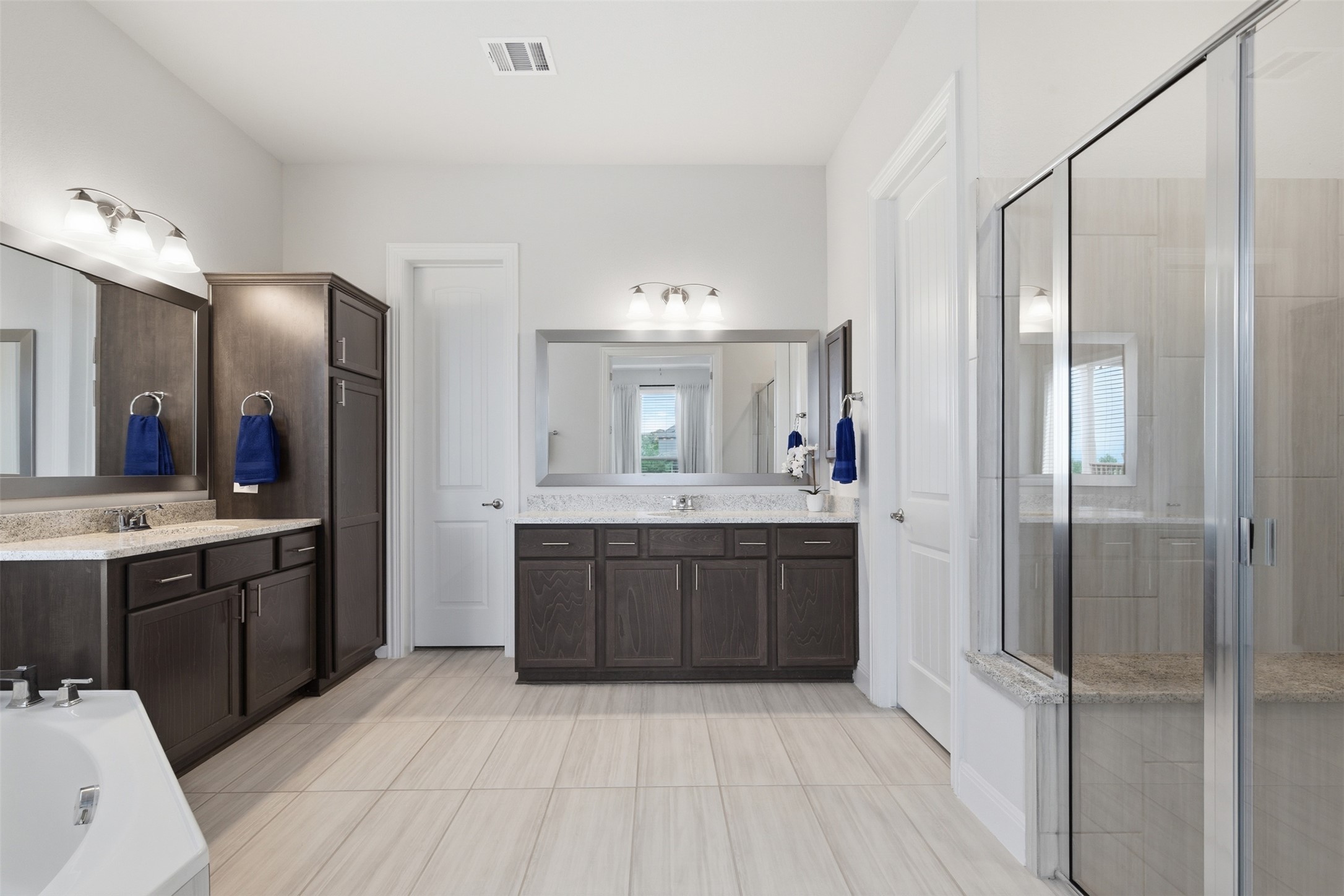 118 Bear Paw Run Georgetown, TX 78628 - Photo 17 of 35 Spacious bathroom featuring light-colored floor tiling, dark wood vanities with light stone countertops, and a clear glass shower enclosure