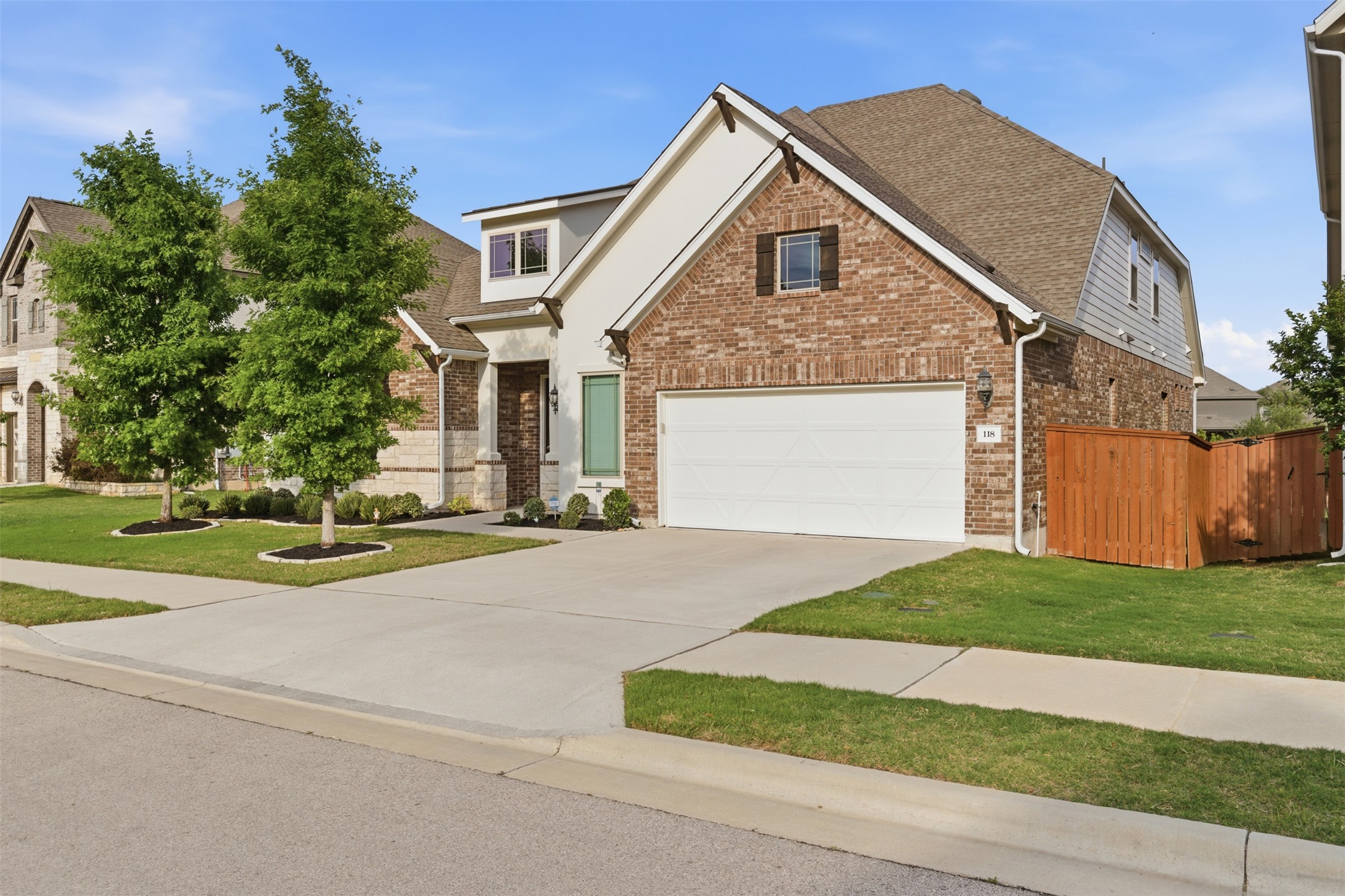 118 Bear Paw Run Georgetown, TX 78628 - Photo 2 of 35 The property features a brick and white facade, a two-car garage, and a well-maintained lawn with mature trees and landscaping