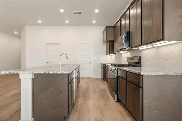 a kitchen with granite countertop kitchen island stainless steel appliances a sink stove top oven and cabinets