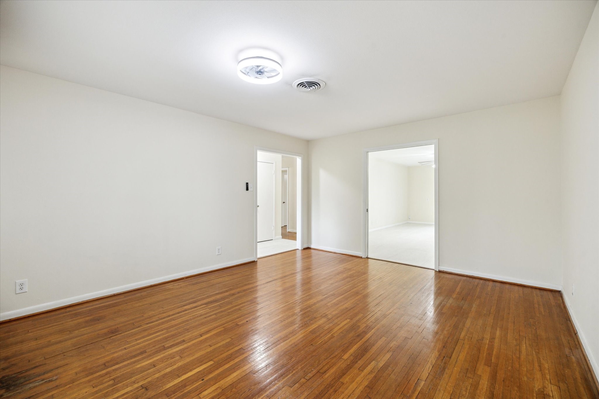 8907 Autauga Street Houston, TX 77080 - Photo 5 of 20 This is a bright, spacious room with polished hardwood floors and neutral-colored walls. It features ceiling lighting and two large doorways leading to adjacent rooms, offering a versatile living space.