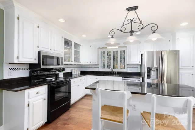 a kitchen with stainless steel appliances granite countertop a sink a stove a refrigerator cabinets and chairs