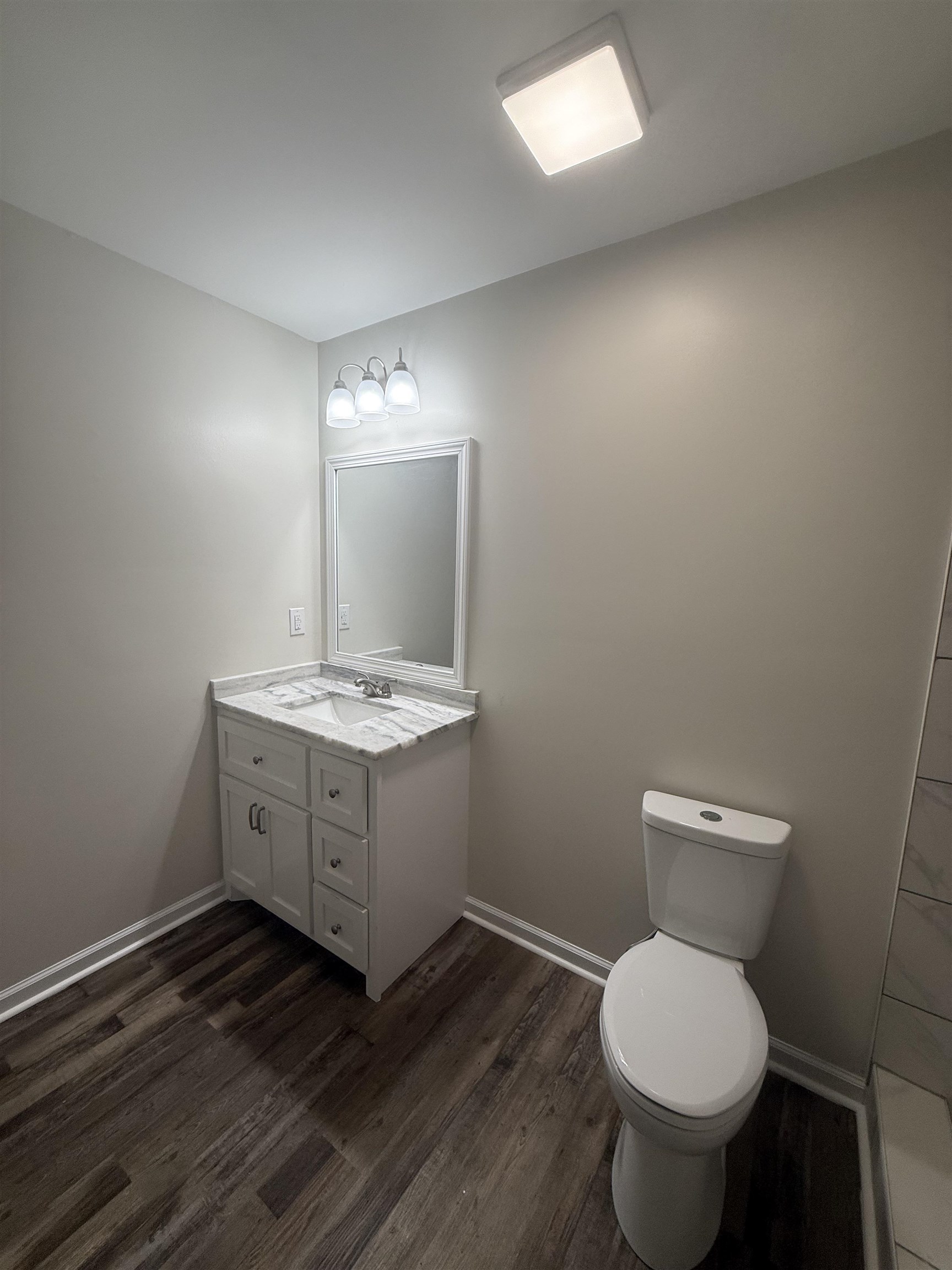 195 Poole Road Moscow, TN 38057 - Photo 11 of 21 Bathroom featuring a white vanity with a marble-patterned countertop, wood-finish flooring, and a contemporary wall-mounted light fixture
