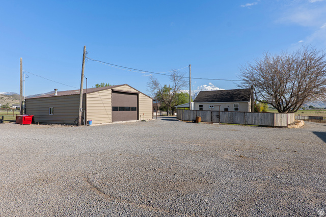 115 East 1600th Street North Santaquin, UT 84655 - Photo 49 of 52 Gravel parking area featuring a large metal-sided outbuilding with a roll-up door and a separate dwelling with light gray siding and a dark roof, partially enclosed by a wood fence