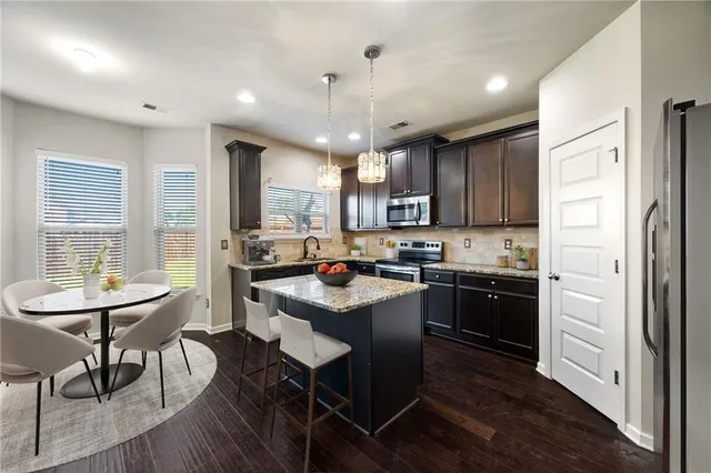 a kitchen with stainless steel appliances granite countertop a kitchen island hardwood floor sink stove dining table and chairs