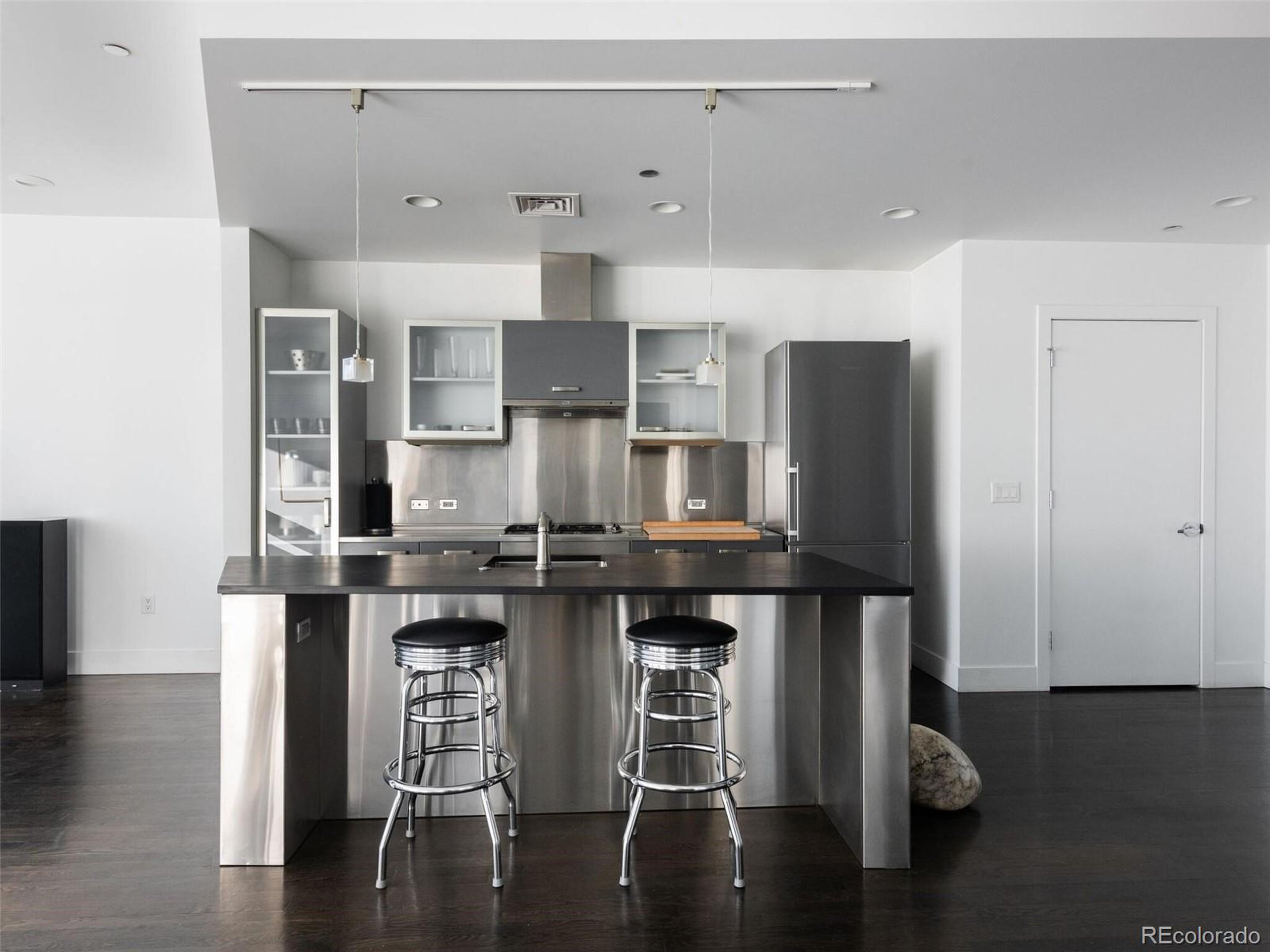 a kitchen with stainless steel appliances a dining table chairs refrigerator and sink