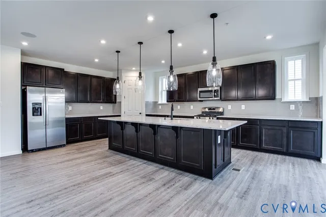 a kitchen with stainless steel appliances kitchen island granite countertop a sink a stove a refrigerator and a oven with wooden floor