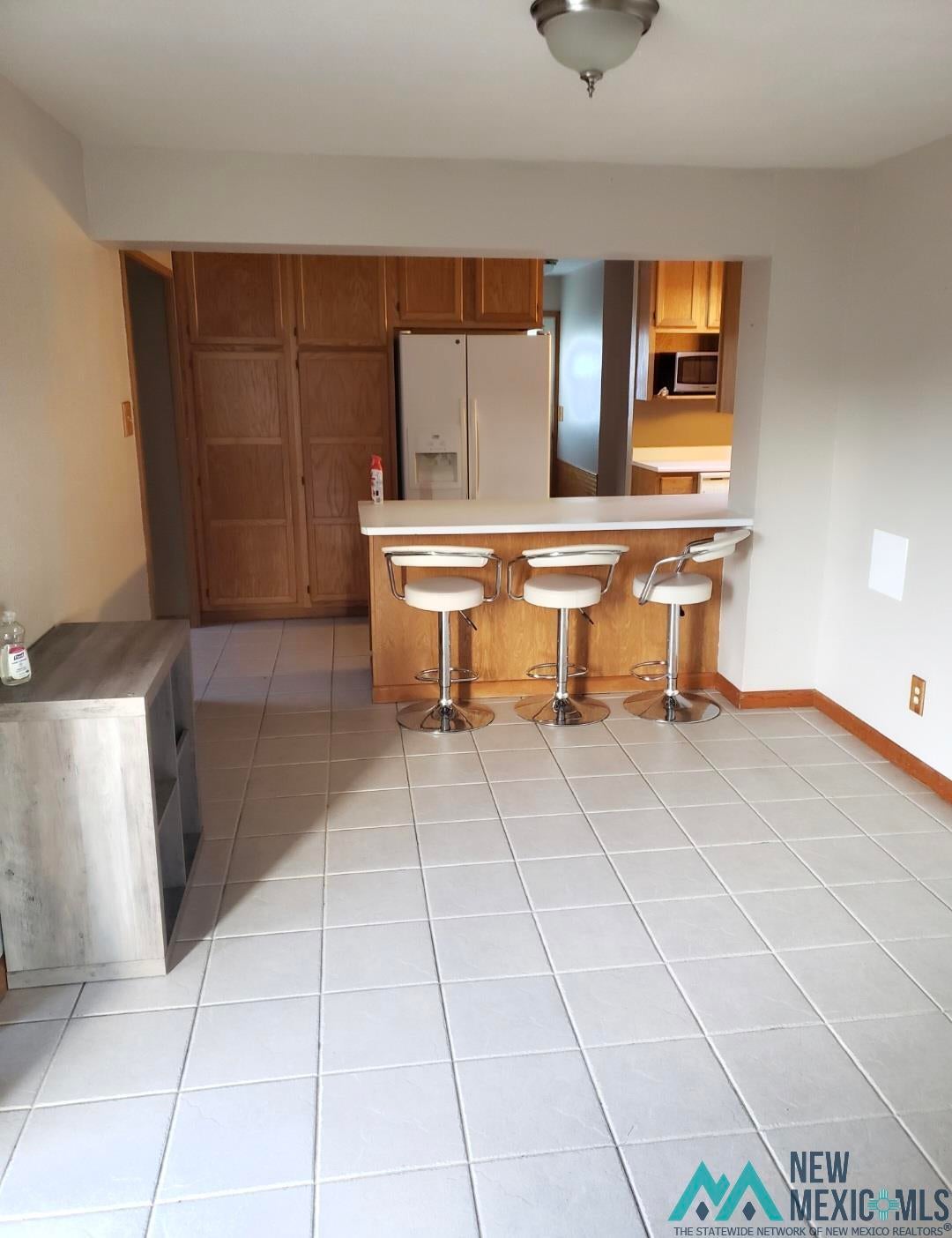 1375 Brilliant Street Raton, NM 87740 - Photo 8 of 19 Kitchen featuring wood finish cabinetry, a peninsula, white fridge with ice dispenser, light tile patterned floors, and a breakfast bar area
