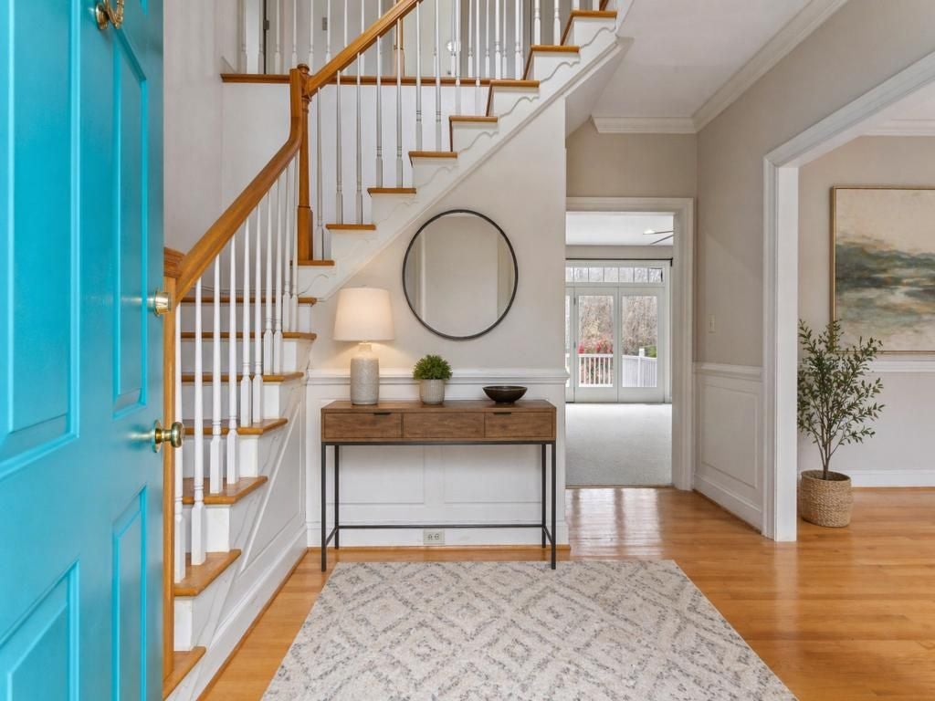 18590 Plank Road Courtland, VA 23837 - Photo 3 of 48 Bright entryway featuring a vibrant turquoise front door, polished hardwood flooring, a classic staircase with wood handrails, white wainscoting, and crown molding