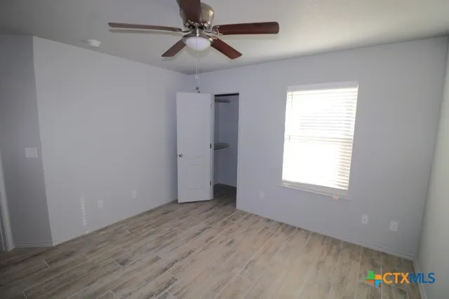 an empty room with wooden floor ceiling fan and windows