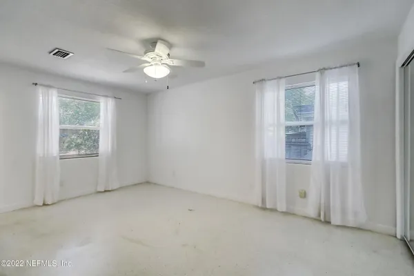 an empty room with chandelier fan and windows