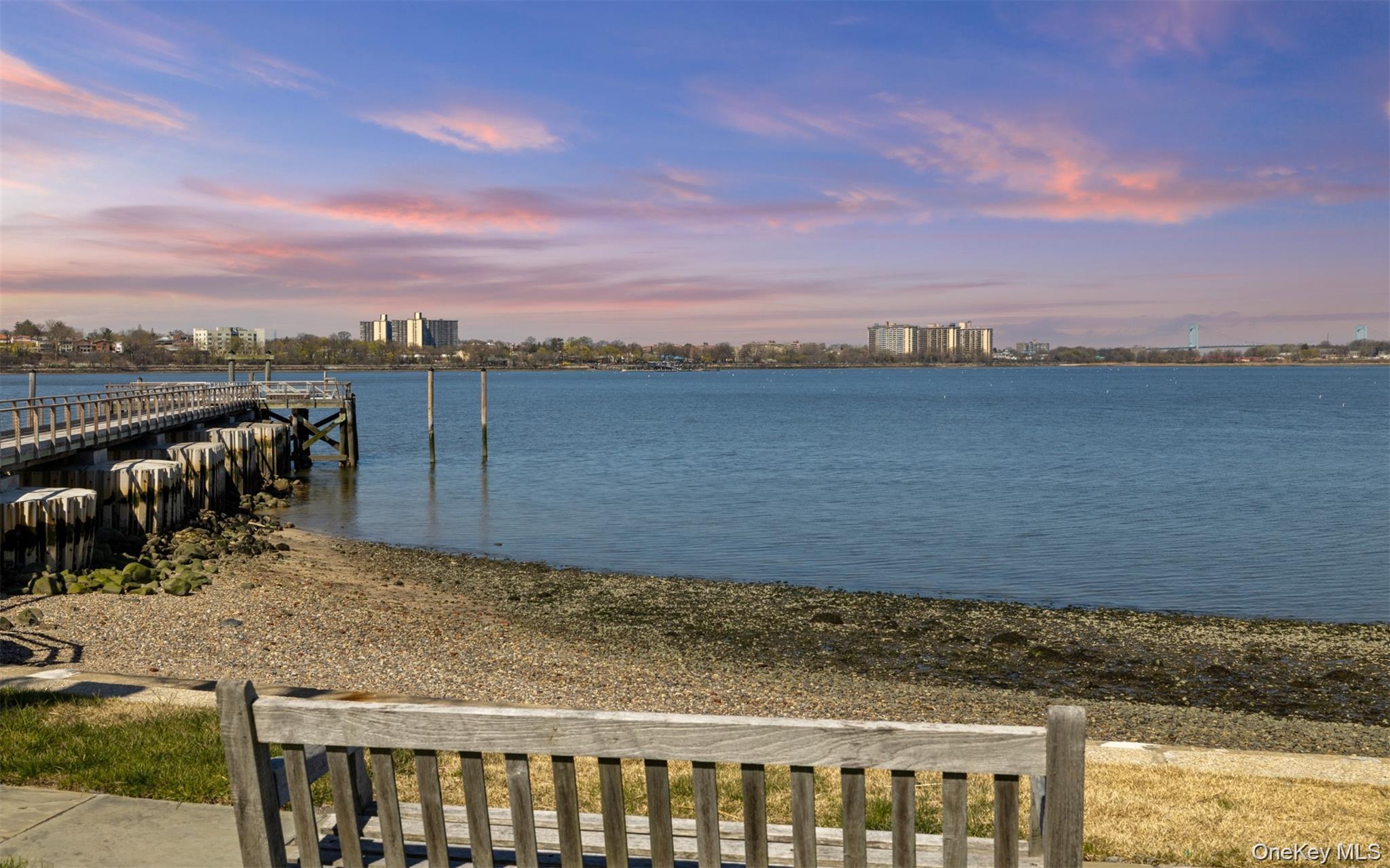 11-20 Shore Road Queens, NY 11363 - Photo 44 of 45 Waterfront setting featuring a wooden pier extending into the water, a natural shoreline, distant city skyline, and a sky with colorful clouds
